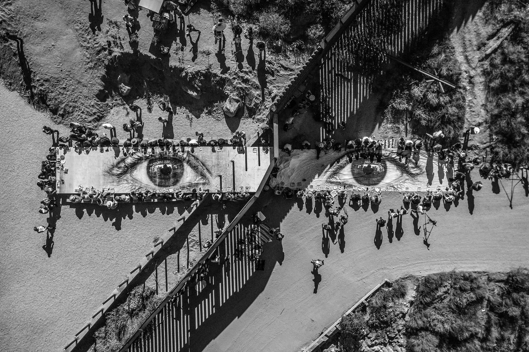 A child's eyes printed on a giant table surrounded by a hundred people on either side of the US/Mexico border