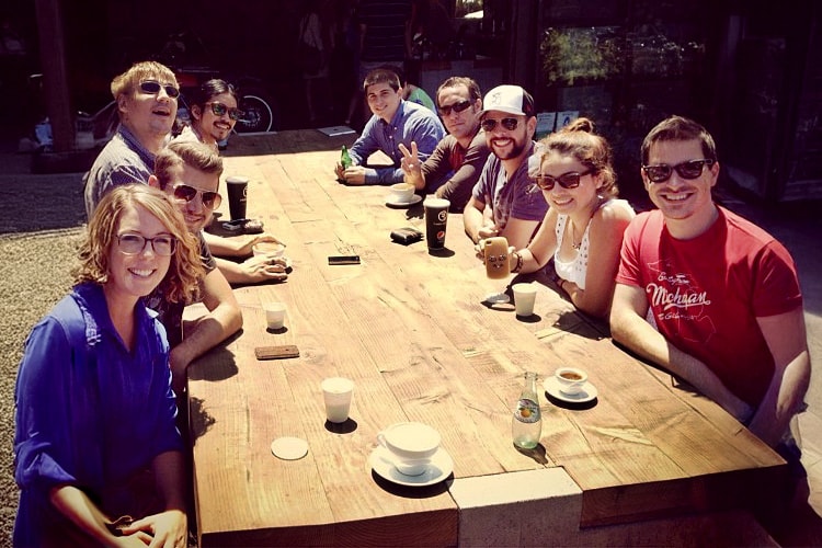 9 people drinking coffee together at a sunny table